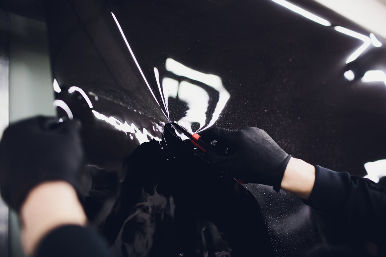 Applying tinting foil on a car window in a garage