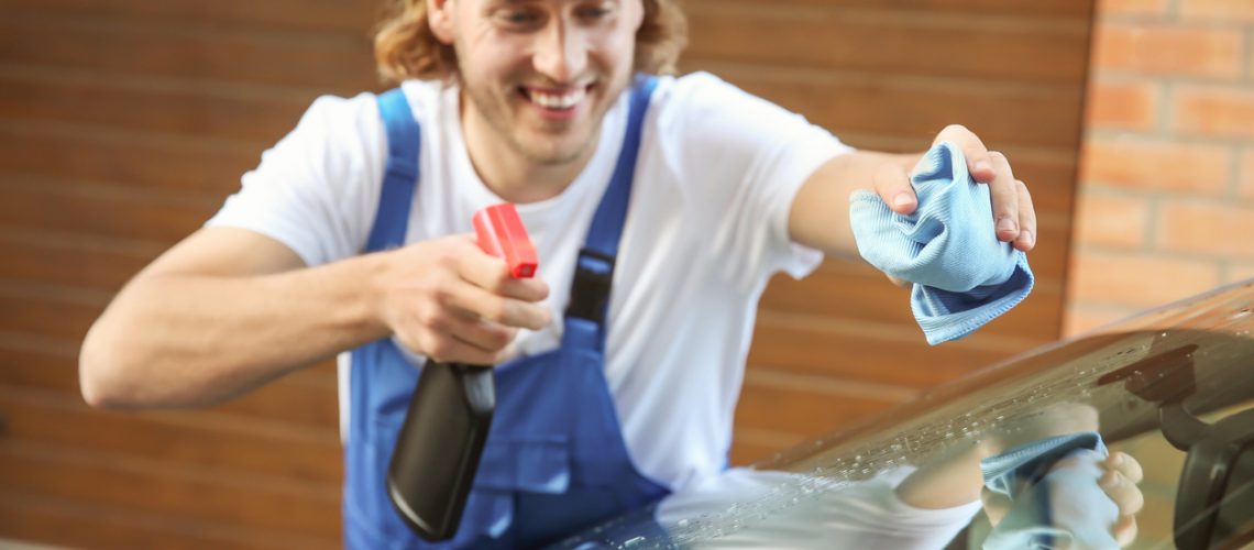Male worker cleaning car window after applying tinting foil outdoors